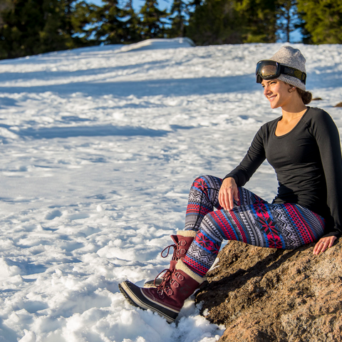 Thermal base layer crewneck top worn by a woman sitting on a rock in a snowy landscape, perfect for winter activities