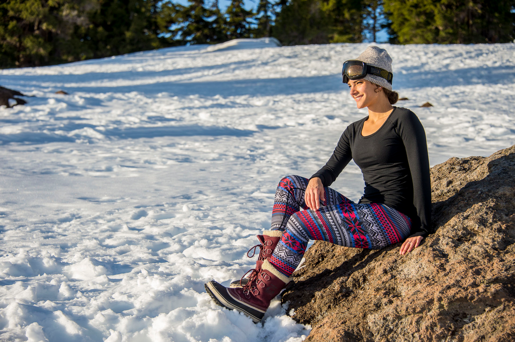 Thermal base layer crewneck top worn by a woman sitting on a rock in a snowy landscape, perfect for winter activities