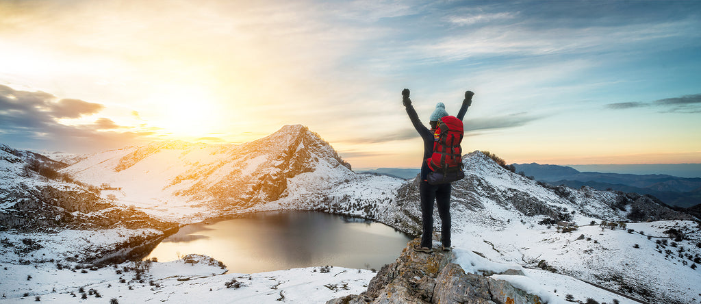 Woman celebrating in nature while wearing womens thermal base layers with a stunning snowy landscape in the background