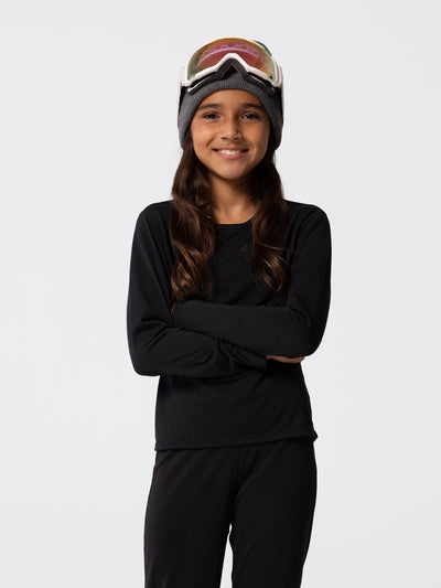 Girl wearing Hot Chillys youth Pepper Skins crewneck and bottom base layer set in black