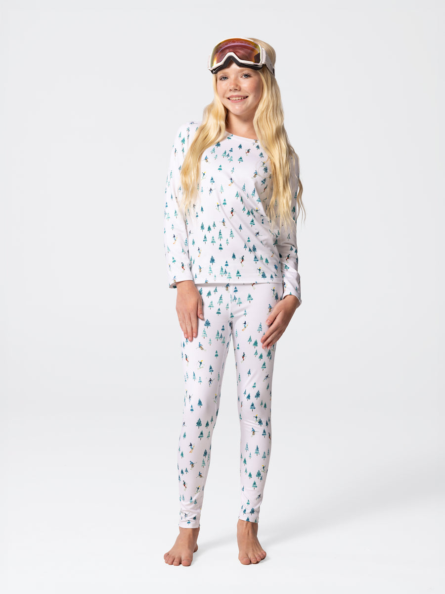 Full-body view of youth wearing Hot Chillys Micro-Elite Chamois Downhill Ski print crewneck top and matching leggings, with ski goggles on head