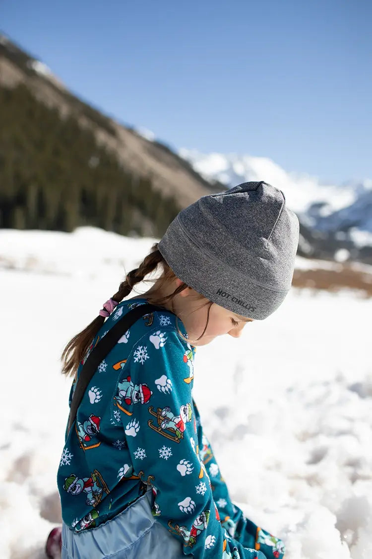 Youth wearing a gray beanie and colorful thermal base layers in a snowy mountain landscape