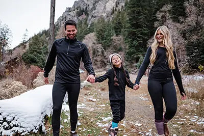 Family of three walking together in a snowy landscape with mountains in the background