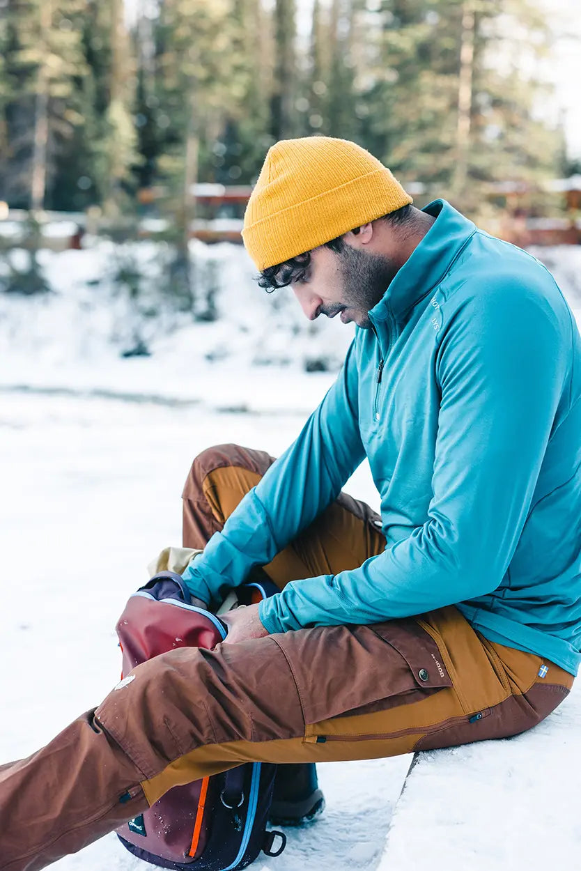 Man wearing Hot Chillys thermal base layers sitting on a snow covered log