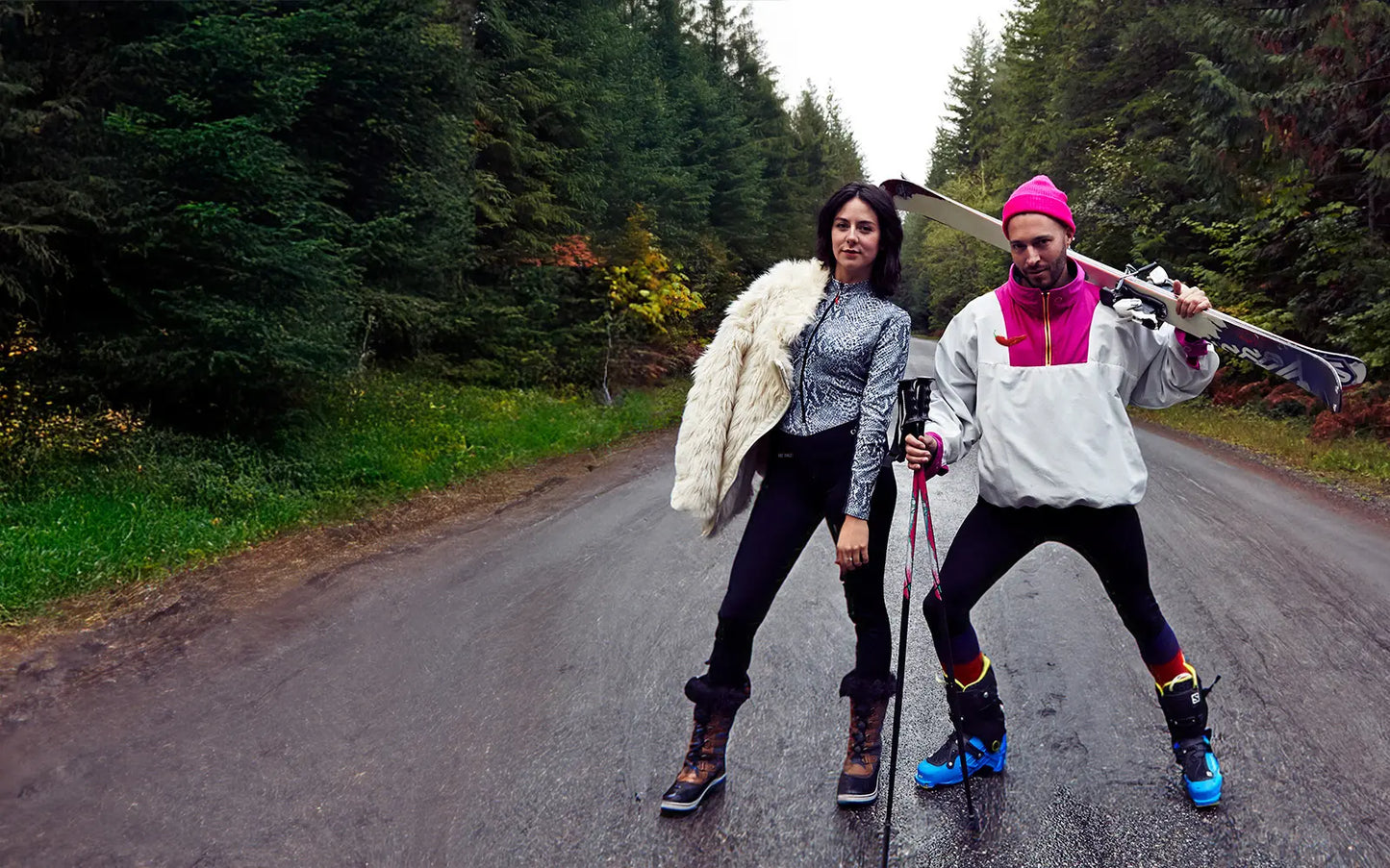 Two people on a forest road with one holding a pair of snow skis.
