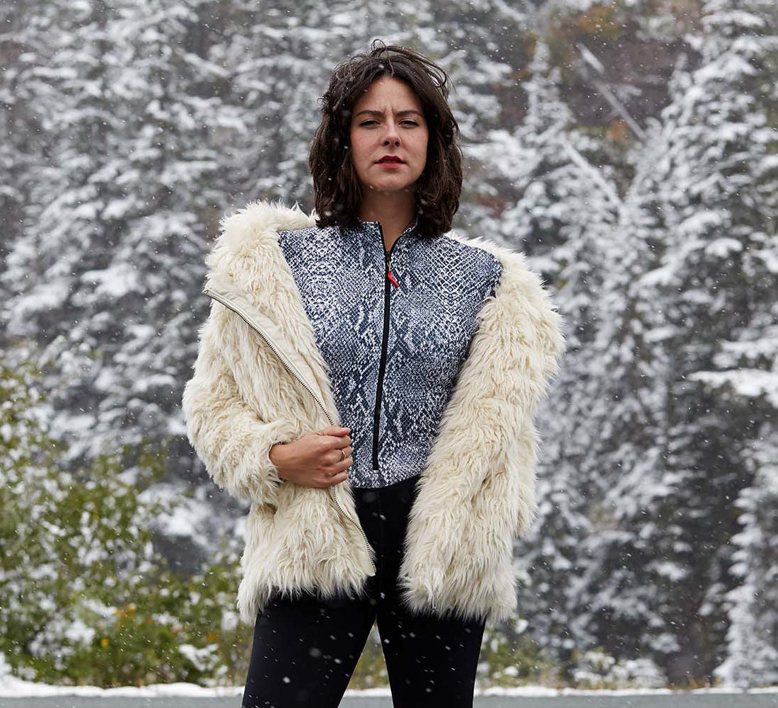 Woman wearing a white fur coat over a retro Hot Chillys patterned jacket in a snowy landscape