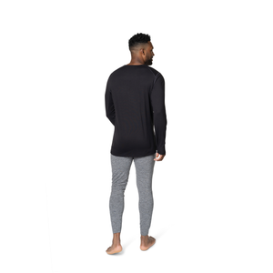 Back view of a man wearing Hot Chillys men's long sleeve thermal top in black paired with gray thermal pants